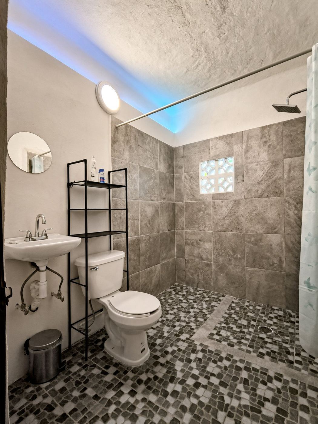 A bath at La Casa Grande, mosaic floor, grey stone shower, and a soft blue light