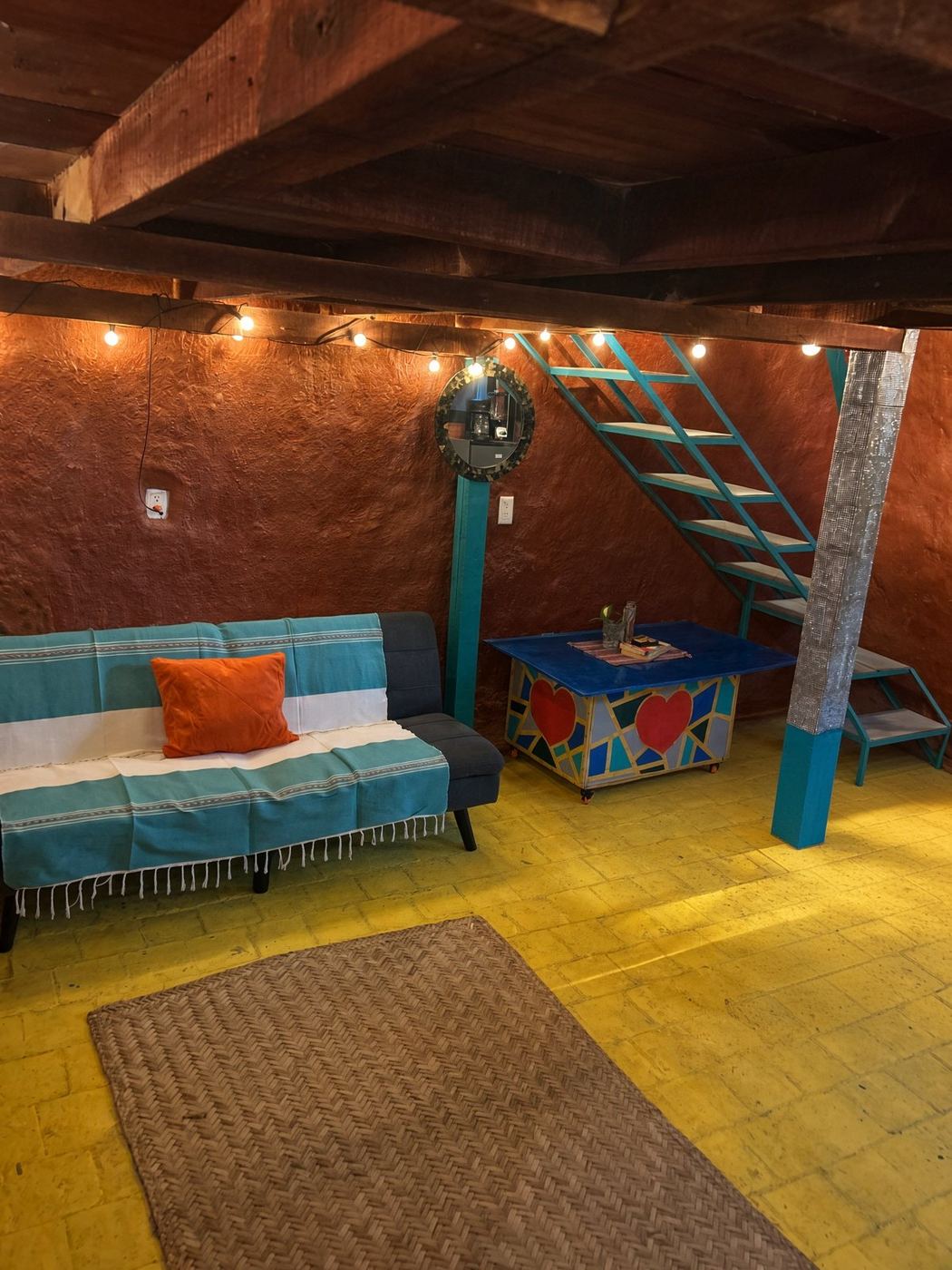 The sofa under the loft, an orange pillow, string lights, and a heart-painted table